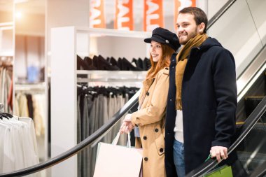 Yakışıklı bir adam ve güzel bir kadın yürüyen merdivende aşağı iniyor.