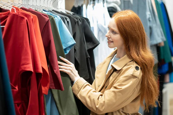 Χαριτωμένη νεαρή καυκάσια γυναίκα επιλέγει ρούχα στο κατάστημα — Φωτογραφία Αρχείου