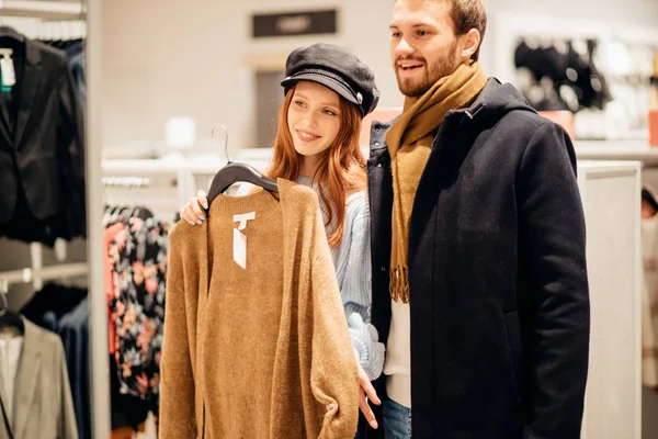 Jovem ruiva mulher à procura de blusa na loja, juntamente com o marido — Fotografia de Stock