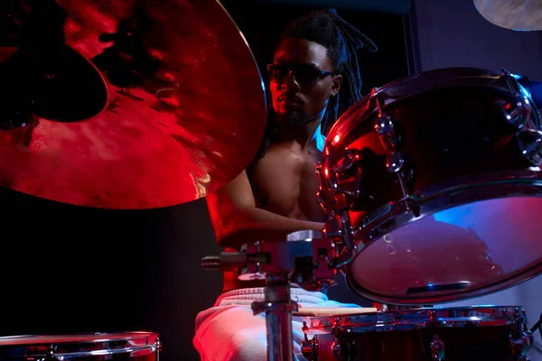 Atractivo hombre africano baterista disfrutando tocando la batería sobre fondo oscuro —  Fotos de Stock