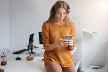 Şirin, genç, beyaz bir yönetici. Ofisinde akıllı telefon ve kulaklıkla oturuyor.