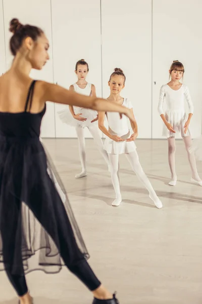 穿着黑色短裙的迷人纤细芭蕾舞演员向孩子们展示芭蕾的正确姿势 — 图库照片