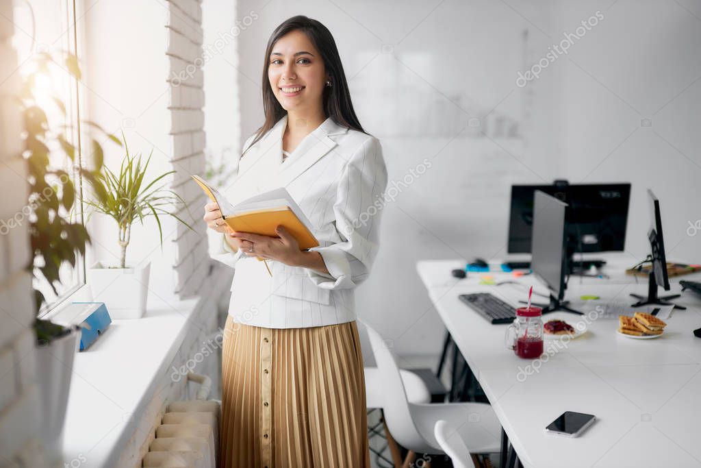 Smiling cute business female with book in office
