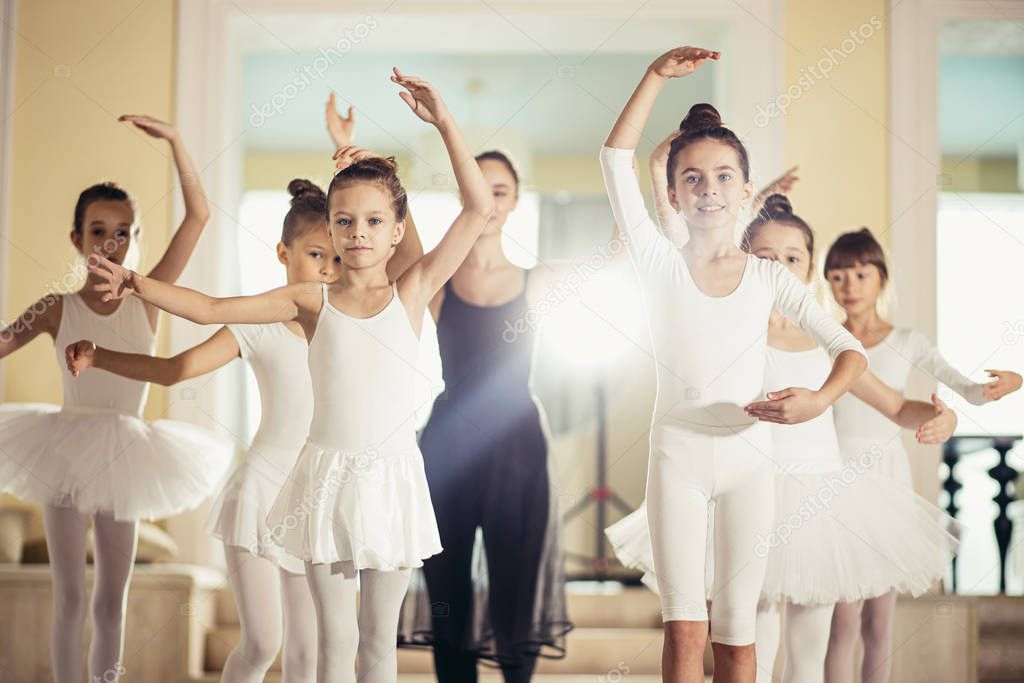 young female ballerina show right pose to kids in studio