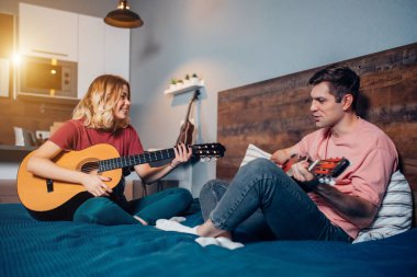 Güzel kız ve yakışıklı adam evde birlikte gitar çalıyorlar.