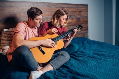 Güzel kız ve yakışıklı adam evde birlikte gitar çalıyorlar.