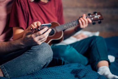 Genç çift ya da arkadaşlar cep telefonuyla nasıl ukulele çalındığına bakıyor.