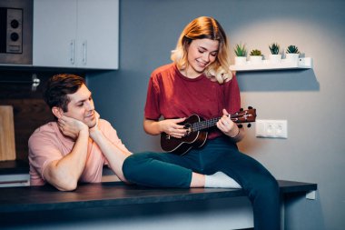 Genç beyaz kadın evde ukulele oynuyor.