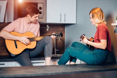 Kafkasyalı çift evde gitar ve ukulele çalıyor.