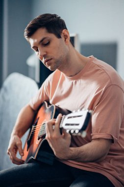 Gündelik gömlekli gitarist yatakta gitar çalıyor.