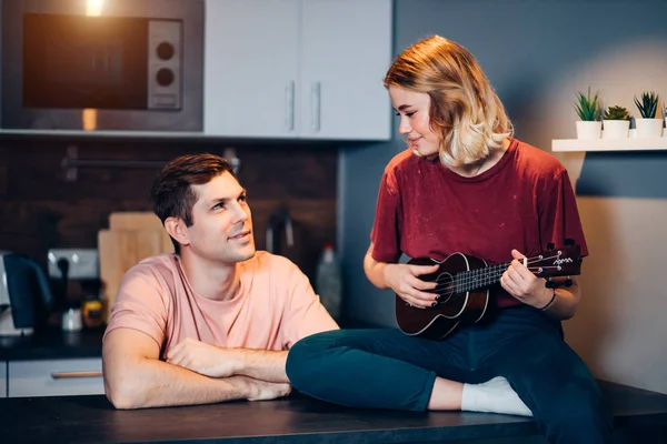 young caucasian woman playing ukulele while his friend listen to her at home