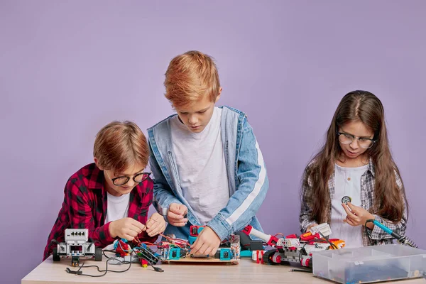 Три концентрированных ребенка собирают игрушки роботов — стоковое фото