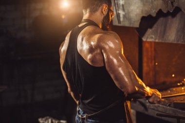 Kafkasyalı genç demirci demircideki erimiş metali dövüyor.