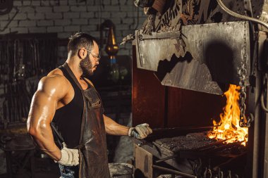 Kafkasyalı genç demirci demircideki erimiş metali dövüyor.