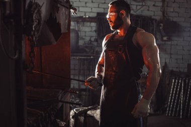 Kafkasyalı genç demirci demircideki erimiş metali dövüyor.