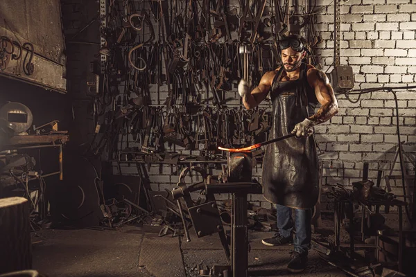 Genç beyaz adam sıcak metali dövüyor.