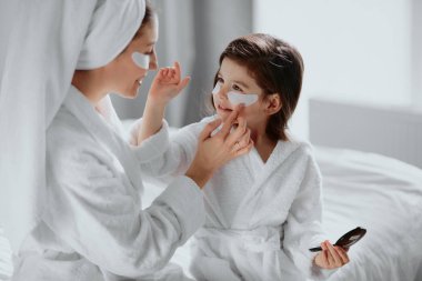careful mother and daughter use facial patches under eyes clipart