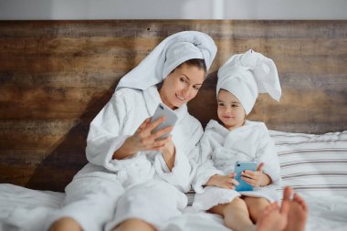 Sevimli anne ve kızı evde akıllı telefon kullanıyor.