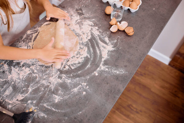 kid rolling dough with rolling pin in kitchen