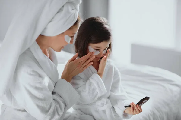 Schattig aangenaam middelbare leeftijd moeder en haar dochtertje in badjas en masker — Stockfoto