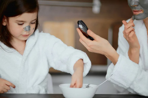 Krásný rodič a jeho dcera sedí v kuchyni s obličejovými maskami — Stock fotografie