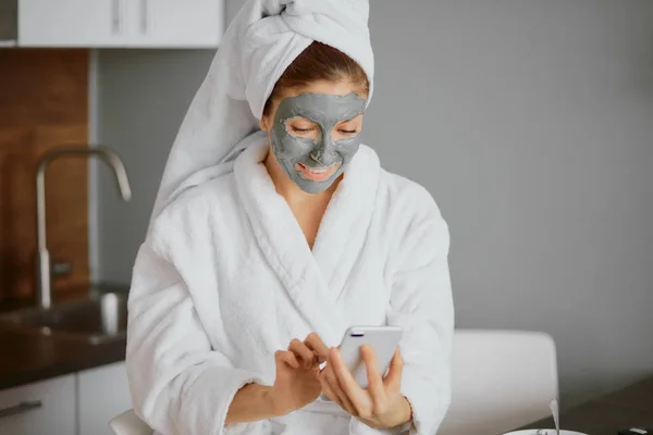 Schöne kaukasische junge Frau mit Gesichtsmaske Blick auf Bildschirm des Mobiltelefons — Stockfoto