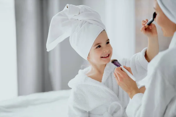 Encantadora niña aplicando maquillaje con cepillo a la madre — Foto de Stock