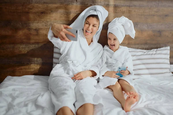 Hermosa hembra y su hija tomando fotos de sí mismos en la cama —  Fotos de Stock