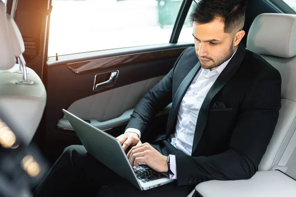 Bärtiger junger Mann arbeitet während der Autofahrt am Laptop — Stockfoto