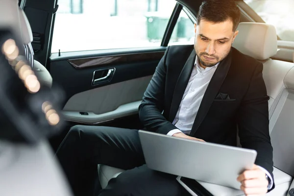 Personable man surfing the Net on laptop while sitting in car