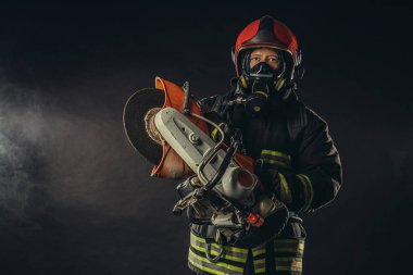 Elektrikli testereli itfaiyeci dumanlı arka planda izole edilmiş.