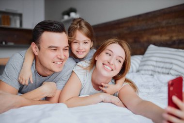 Mutlu gülümseyen aile yatakta selfie çeker.