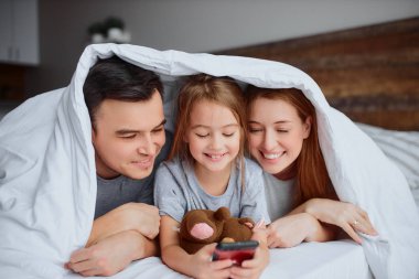 Modern gülümseyen beyaz aile yatağında akıllı telefonuyla