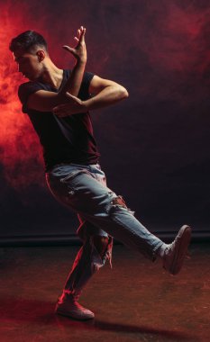 Smoky Stüdyoda izole edilmiş çeşitli adımlar gösteren kot giyen bekar genç bir dansçı.