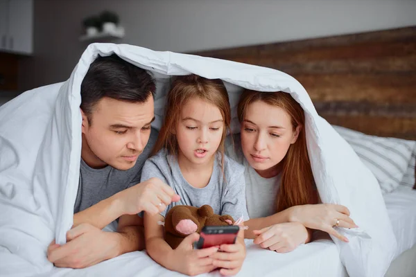 Moderne Kaukasische familie met smartphone op bed — Stockfoto