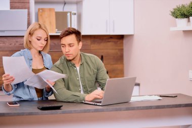 caucasian young spouses sitting with laptop and documents at home clipart