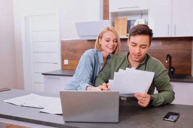 Gülümseyen çift evde dizüstü bilgisayar kullanarak birlikte oturuyorlar.