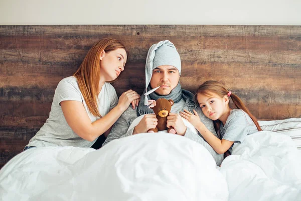 У батька є температура, що лежить на ліжку з дружиною і дитиною — стокове фото