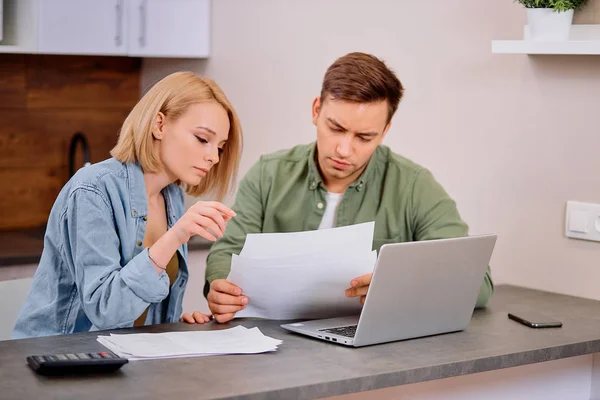 Kaukasiskt ungt par läser och analyserar räkningar sitter vid bordet — Stockfoto