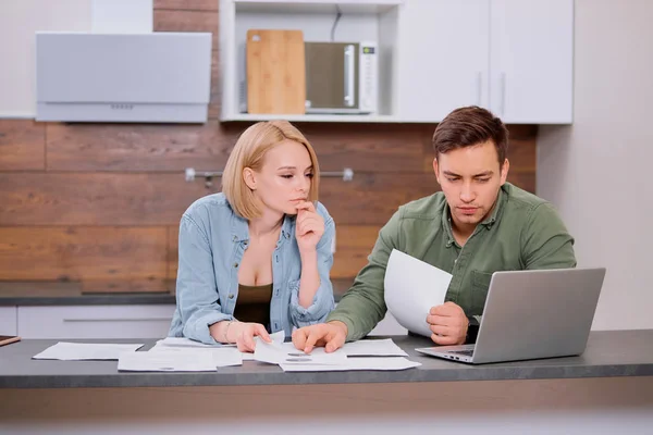 Verbaasde getrouwde man en vrouw zitten samen aan tafel met laptop — Stockfoto