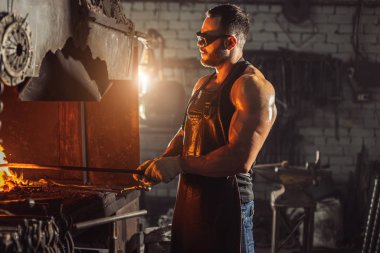 Ciddi vahşi kaslı demirci ocakta demiri ısıtıyor.