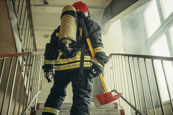 Bombeiro caucasiano com martelo arriscando sua vida para salvar as pessoas do fogo — Fotografia de Stock