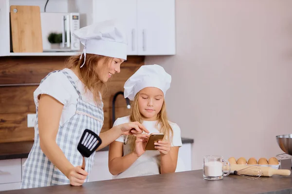 Kvinna och barn titta på smartphone innan bakning — Stockfoto