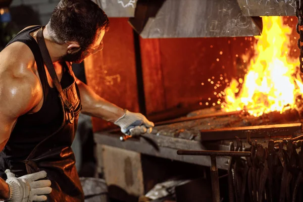 Young traditional caucasian blacksmith working with open fire in workshop — Stock Photo, Image