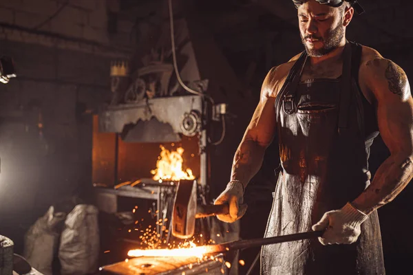 Mladý kovář mlátící železo kladivem — Stock fotografie