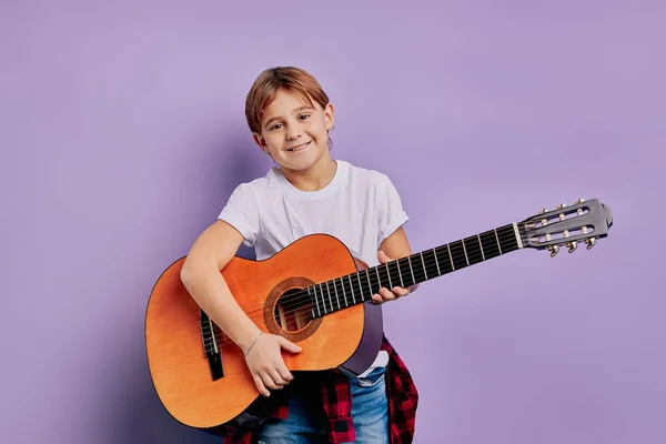 Улыбающийся мальчик, играющий на гитаре на фиолетовом фоне — стоковое фото