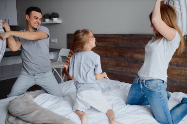 Neşeli beyaz anne baba ve çocuk yastıklarla kavga ediyor.