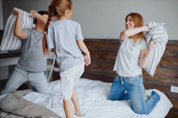 Кавказские родители и ребенок веселятся с подушками на кровати — стоковое фото