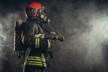 Dumanlı arka planda üniformalı itfaiyeci.