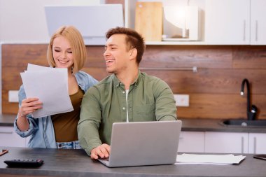 Heyecanlı genç adam ve kadın evde dizüstü bilgisayar kullanıyorlar.